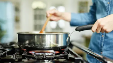 Getty Images Close-up midsection image of woman cooking food in frying pan. Utensil is placed on gas stove.