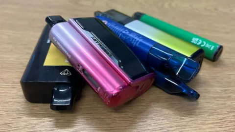 BBC A pile of disposable vapes on a table. They are 