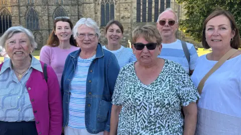 Five women and one man stand in a group outside the front of Durham Cathedral.