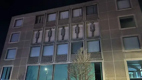 Night image of Grimsby Central Library showing the five sculptures mounted on the wall 