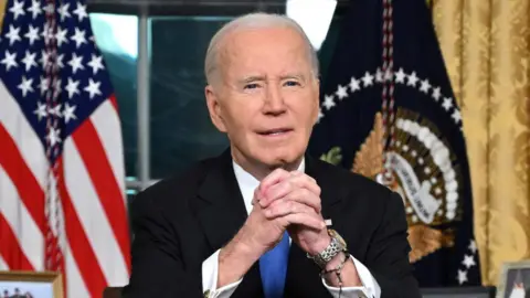 President Biden sits at his desk in the Oval Office.