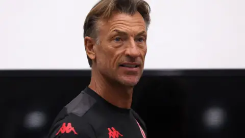 Herve Renard, visible from shoulders up, wears a wearing a black Tunisia training top as he looks over his right shoulder towards the camera