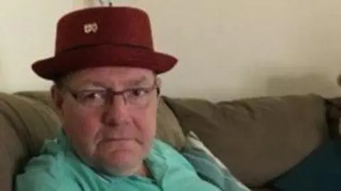 Leicestershire Police Gary sits on a sofa wearing a red hat 