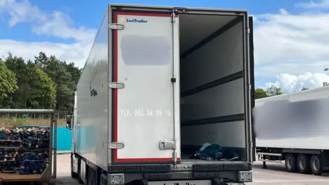 BBC A large white lorry with one of its back doors open, showing sleeping bags on the bed of the lorry.