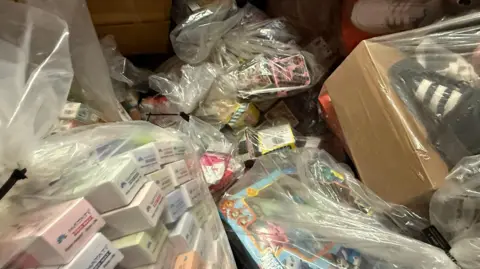 Bags of fake counterfeit items from illegal cigarettes to children's toys. A selection of shoes can also be seen in the right hand corner.