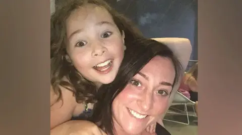 Milly Main smiling while looking at the camera. She has long brown hair. She is on the back of Kimberly Darroch, who has long black hair and is also smiling at the camera.