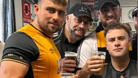 Joe Greenham Kieran Greenham (left) pictured with his father, Tony, and brothers Joe and Aidan. They are holding drinks and wearing Hull City scarves and shirts. 