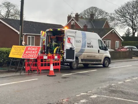 BBC News A van is parked on a road with signs and traffic cones and a 'Road Ahead' closed sign as repairs to the cables continue 