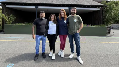 Sergio, Alex Aguariar, Lauren and Ben King demonstrates a photo in the middle of the stadium at the Churchown Elementary School. They stand near each other and get their arms around each other.