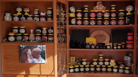 Marmite jars and memorabilia on shelves in a house, with a photo of David and Laura Walker also on the side