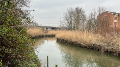 A river passes next to some flats and a road bypass