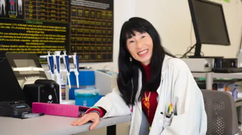 Wayne State University Wearing a lab coat, Tamara Hew-Butler sits at a desk in a laboratory.