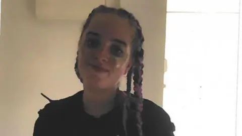 Tasha Ashby, with long coloured plaits and wearing a dark top is pictured smiling.