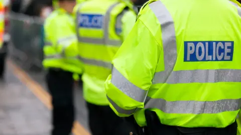 Getty Images Three police officers wearing black trousers and yellow hi-vis jackets which say 'police' across the back in reflective silver letters.