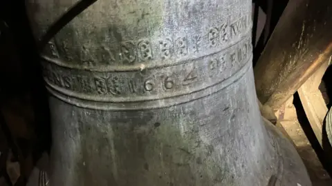 A bell with '1664' written on the side with a grey colouring to the bell.