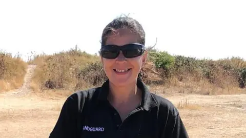 Contributed Leonie Washington smiles at the camera while standing on a beach. She has dark hair that has been tied back and wears sunglasses with a black polo T-shirt.