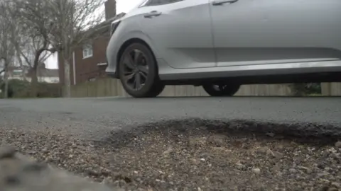 Local Democracy Reporting Service/Oliver Leader de Saxe A large pothole on a residential road. There is a white vehicle parked beside the pothole.