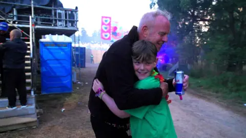 Rob Williams A man with grey hair and black jacket hugs a young boy with brown hair and green T-shirt.