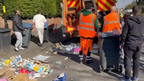 People gather around a refuse lorry in the streets of Birmingham