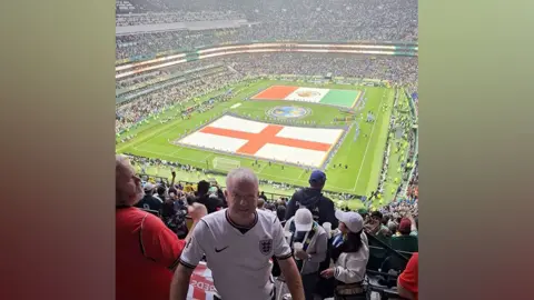 Paul Clegg Paul Clegg inside the stadium. He is in the stands and behind him is the pitch with the England and Mexico flags across the grass. The stadium is packed with thousands of fans