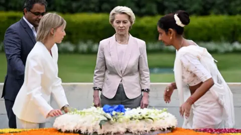 European Commission President Ursula von der Leyen pays respect at Mahatma Gandhi memorial at Raj Ghat in New Delhi on February 27, 2025. She is wearing a cream coloured blazer and is surrounded by three other officials. 