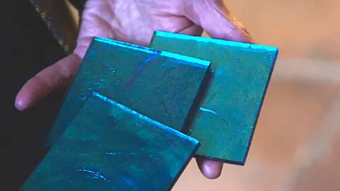 A hand holds three glass tiles in shades of shimmering blues.