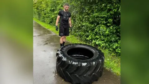 Will Fraser-Coombe stood in front of a large black tyre