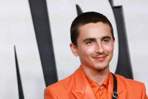 Timothée Chalamet wears an orange shirt and orange jacket on the red carpet.