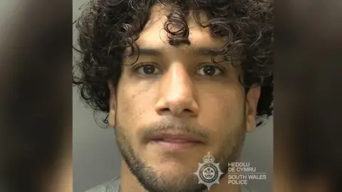 Najib Arab mugshot. He has curly black hair and stubble. 