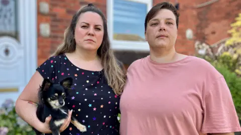 Dos mujeres y un perro pequeño afuera de una casa.