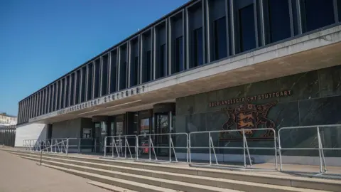 Getty Images A brutalist building with green and grey stone walls with a gold emblem on the side reading Oerlandesgericht Stuttgart 