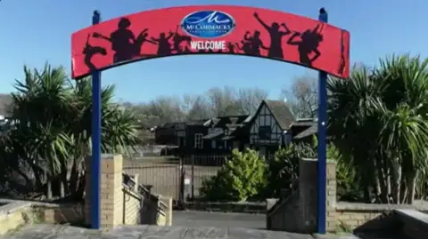 BBC The entrance sign to the former Pleasure Island with steps going down, trees either side and old buildings in the distance 
