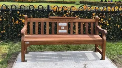 A bench placed on a concrete slab. It is placed in front of a metal fence.