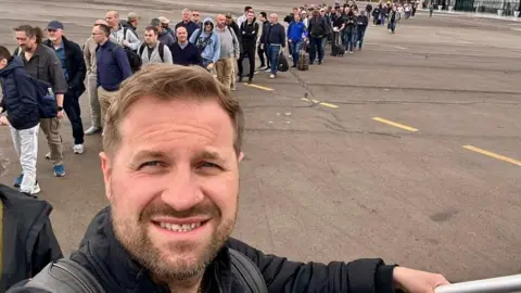 Ross Slater A man with a beard boards a plane outside with a queue of people behind him