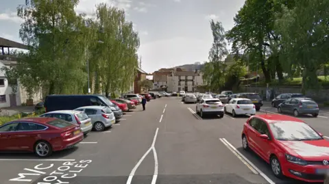 Court Ash Car Park in Yeovil with lots of cars, weeping willow trees and a member of the public in the distance