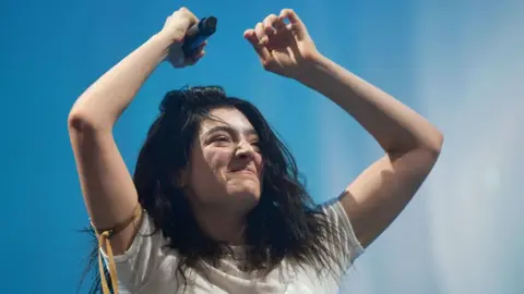 Lorde with her arms raised on stage at Glastonbury