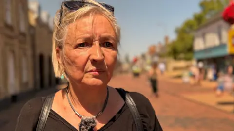 Jane Coles wearing a brown top, standing in a street