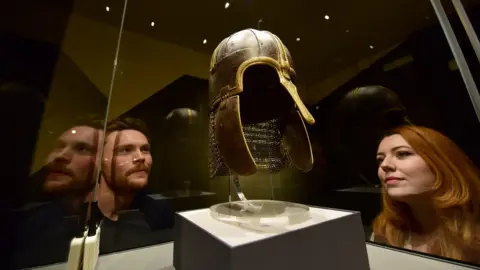 A man and woman look into a glass case displaying an iron and bronze helmet.