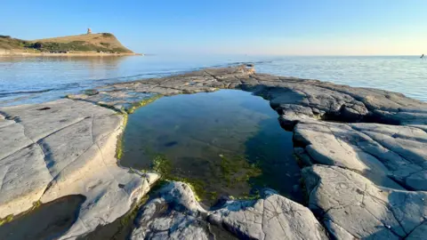 BBC Weather Watcher Dee Cee Kimmeridge, Dorset large flat rock pool overlooking the sea and coastline t the left.