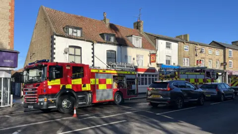 John Devine/BBC Two fire engines parked up on the High Street next to the lane entrance. They are outside a pub.