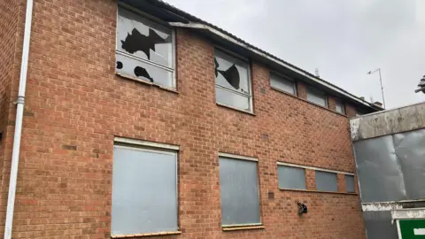 A disused home on Hospital Close in Leicester with two of the upper floor windows smashed by vandals. The lower windows are covered with protective metal sheets. 