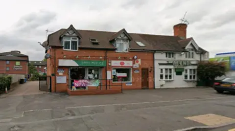 A building in the middle of the photo has the words post office in white on a green backing and to the right of that is a yellow and red post office logo.