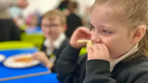 Generic image of a little girl with a blonde ponytail eating toast at a primary school breakfast club