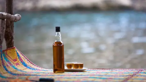 Getty Images An alcohol bottle and shot glasses on at mat.