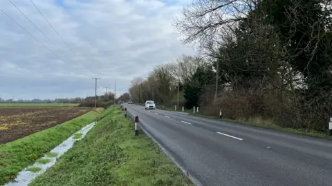 Clare Worden/BBC Pullover Road, which is where the man's body was found. It is a two-lane road with trees overhanging it on one side and a ditch next to farmland on the other
