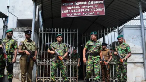 Getty Images Men dressed in camouflage uniform holding rifles in front of metal gates of a court