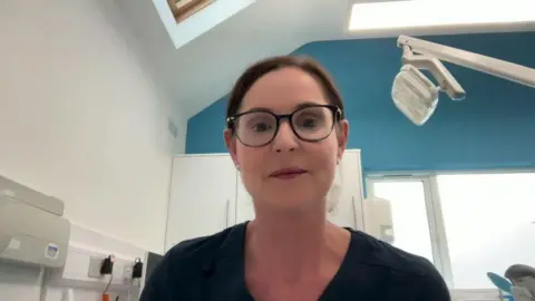 A woman who is wearing glasses and a navy top. She has brown hair.