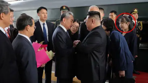 Xinhua Kim shakes an official on the train platform, surrounded by other officials and guards wearing the uniform. His daughter stands behind him and wear a black suit.