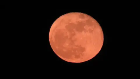 Vista desde mi ventana: Luna llena con un tinte rojizo. Tomada desde Hartlepool. El cielo que rodea la luna está completamente negro.