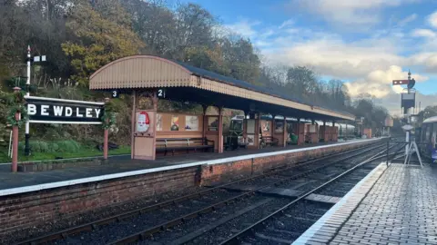 A Bewdley sign is on the platform on the left by a long covered area. A smaller part of the other platform is visible on the right.